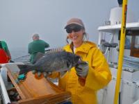 NOAA National Marine Fisheries Service-Sea Grant Fellow Sabrina Beyer stands on a boat holding a rockfish 