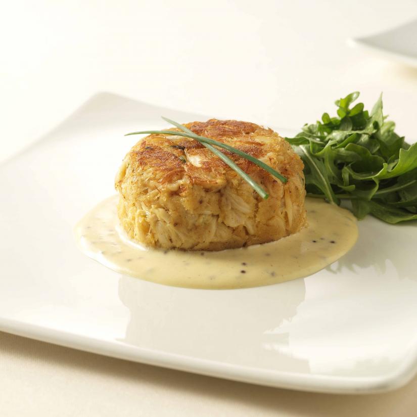 crab cake on top of yellow cream sauce, garnished with salad greens and green onion