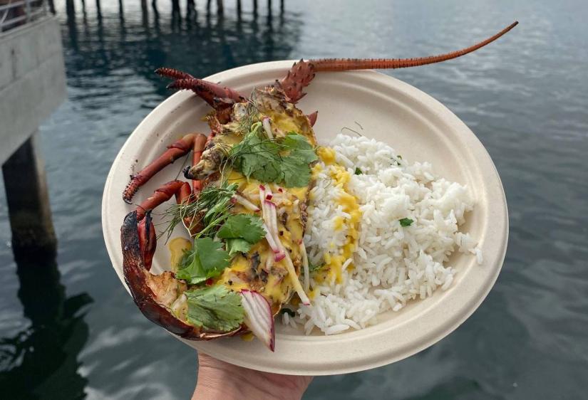 plate of halved lobster with curry sauce and rice with ocean and building in background
