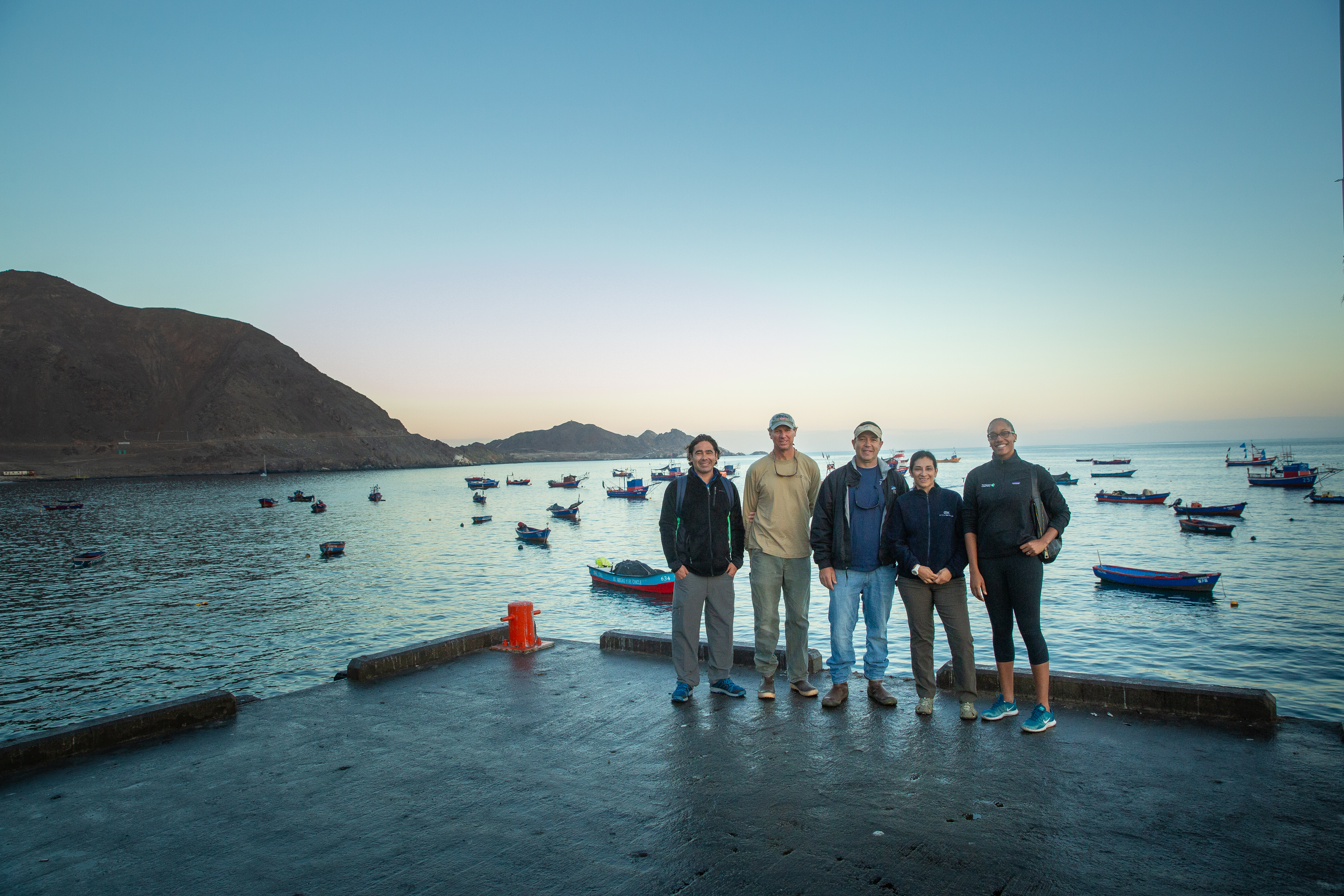 five people standing on a dock in Chile with small boats behind them