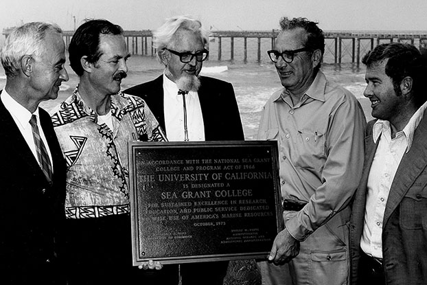 Five men stand with plaque in front of Scripps Pier in black and white photo.