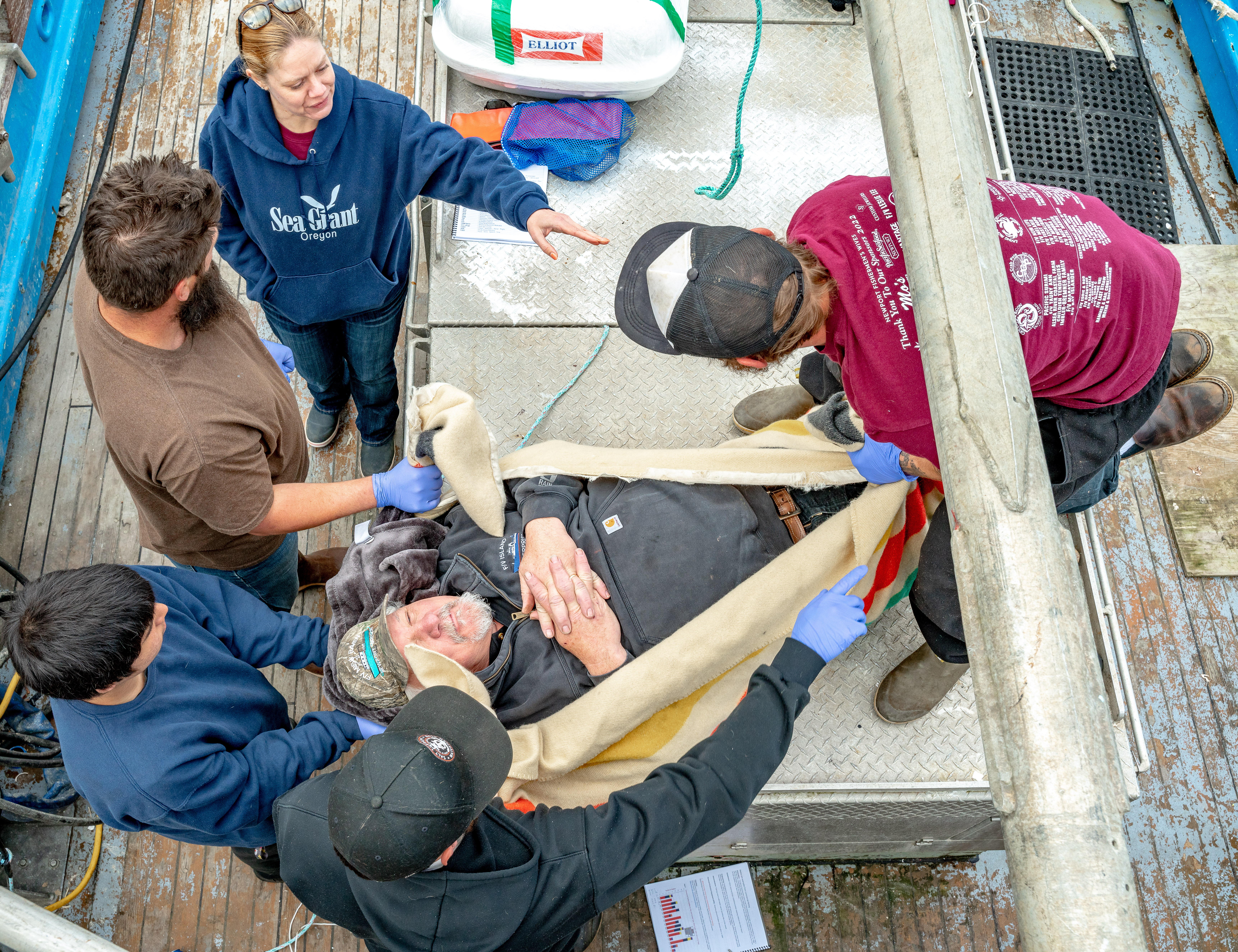 people holding a person pretending to be injured for the training on a boat