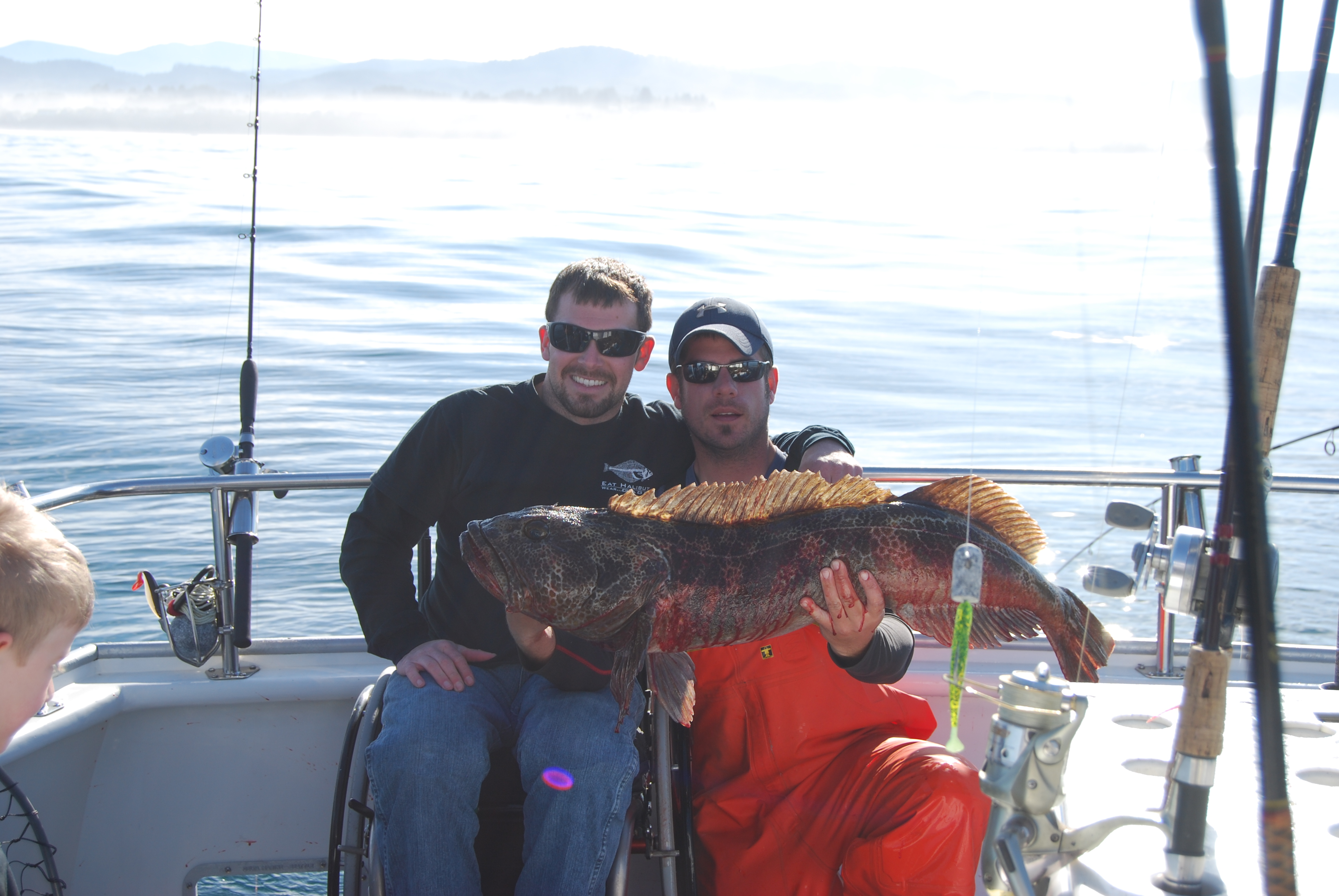 dirtsailor2003/flickr two people holding a lingcod fish aboard a fishing boat with fishing poles, one person is on a wheelchair