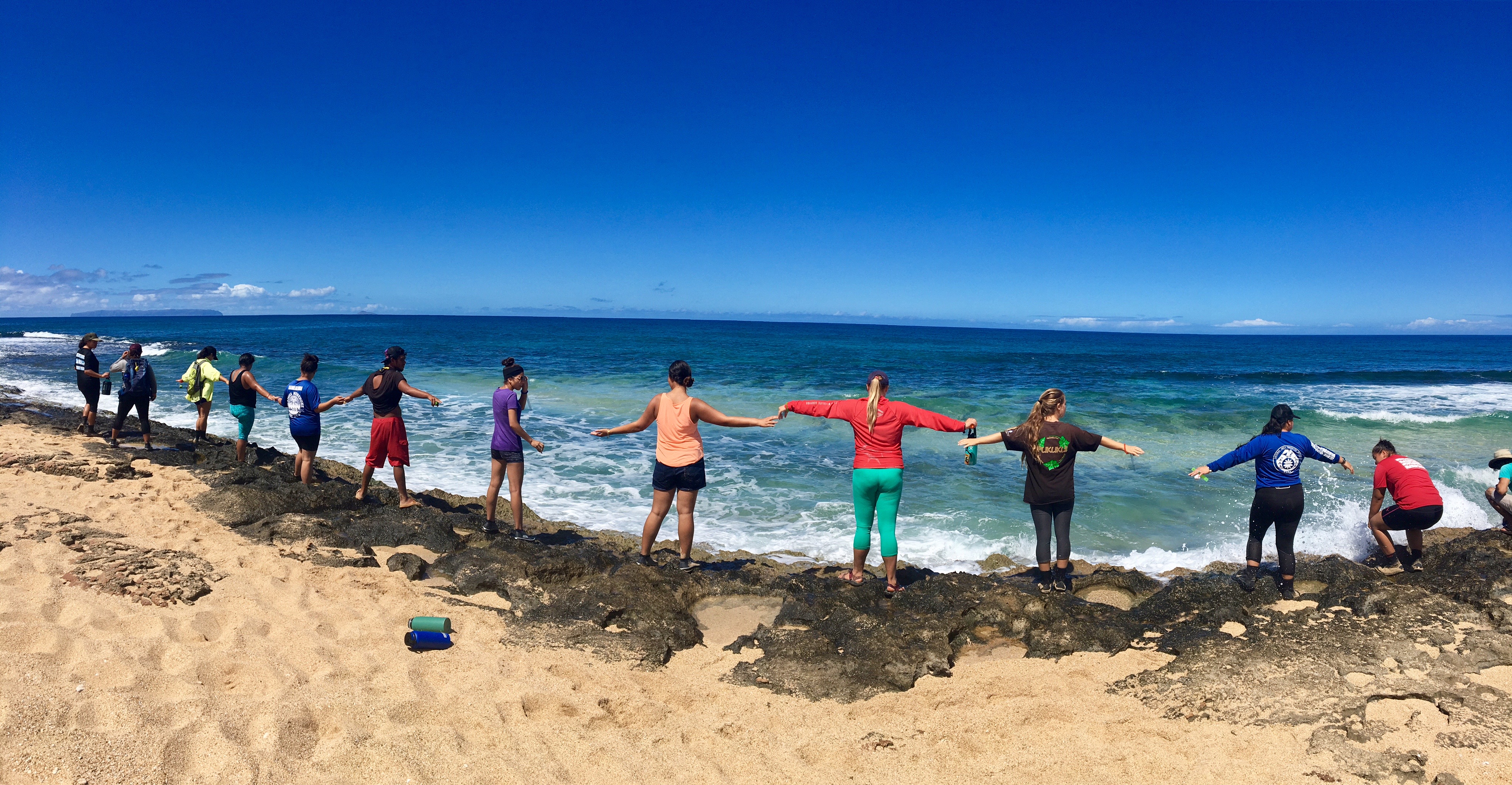 people standing on the coastline with their arms raised to the side