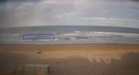 A photo taken from the beach facing the ocean shows the sand leading into the waterand a blue highlighted box outlines a section of the ocean in the waves that identifies a ripcurrent in the water. 