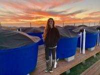 Katie Neylan in front of the tanks holding the sablefish