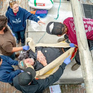 people holding a person pretending to be injured for the training on a boat