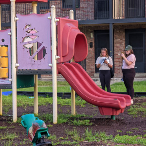 Two people standing next to a pink and red playground slide, recording temperature