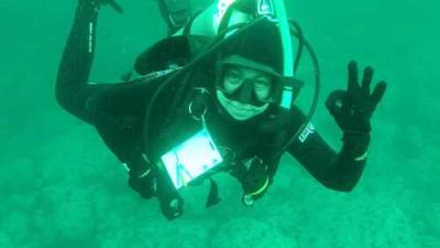 A woman gives the OK sign underwater while scuba diving.