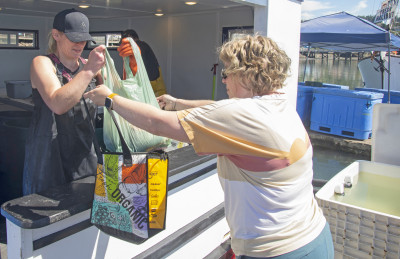 A participant in Oregon Sea Grant's Shop at the Dock tour buys seafood from the Chelsea Rose floating seafood market in Newport on Aug. 4, 2023