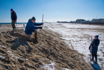 Three volunteers on the beach in New Hampshire holding a sticks with a string attached to both.
