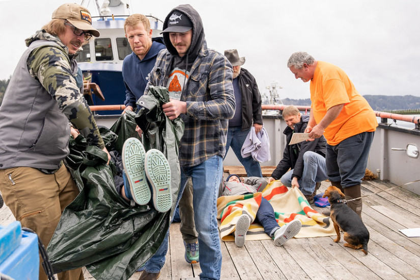 Two groups of fishermen on the deck of a fishing boat practice packaging and carrying an injured crewmate safely. 