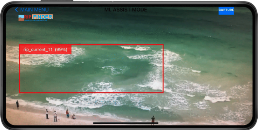 Image of a phone running the RipFinder app. The phone screen is displaying a recording of the shoreline with a rip current outlined by the app's detection bounding box.