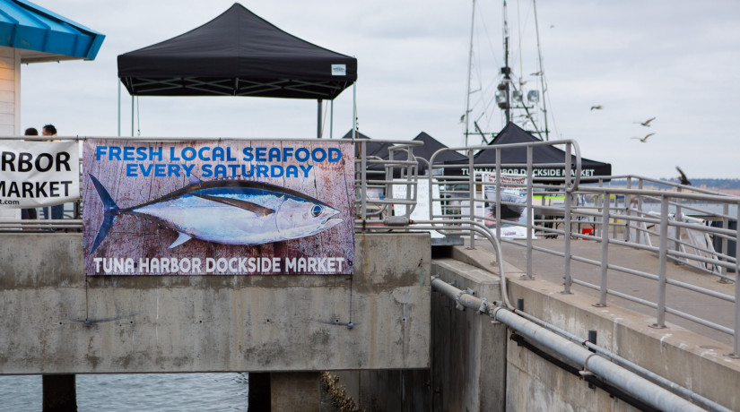 banner for tuna harbor dockside market with vendor tents in background