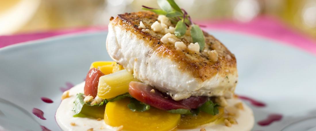 Pacific halibut filet with garnish, cooked vegetables, plated on a cream sauce base, and drizzle of purple-colored sauce of 
