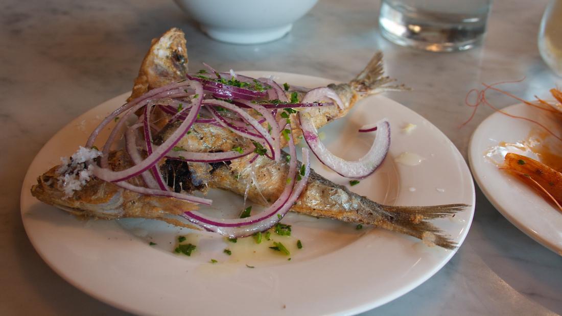 Fried sardines garnished with red onion and greens.