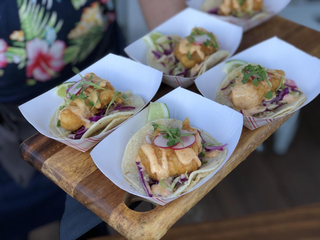 Five paper plates with fried fish tacos.