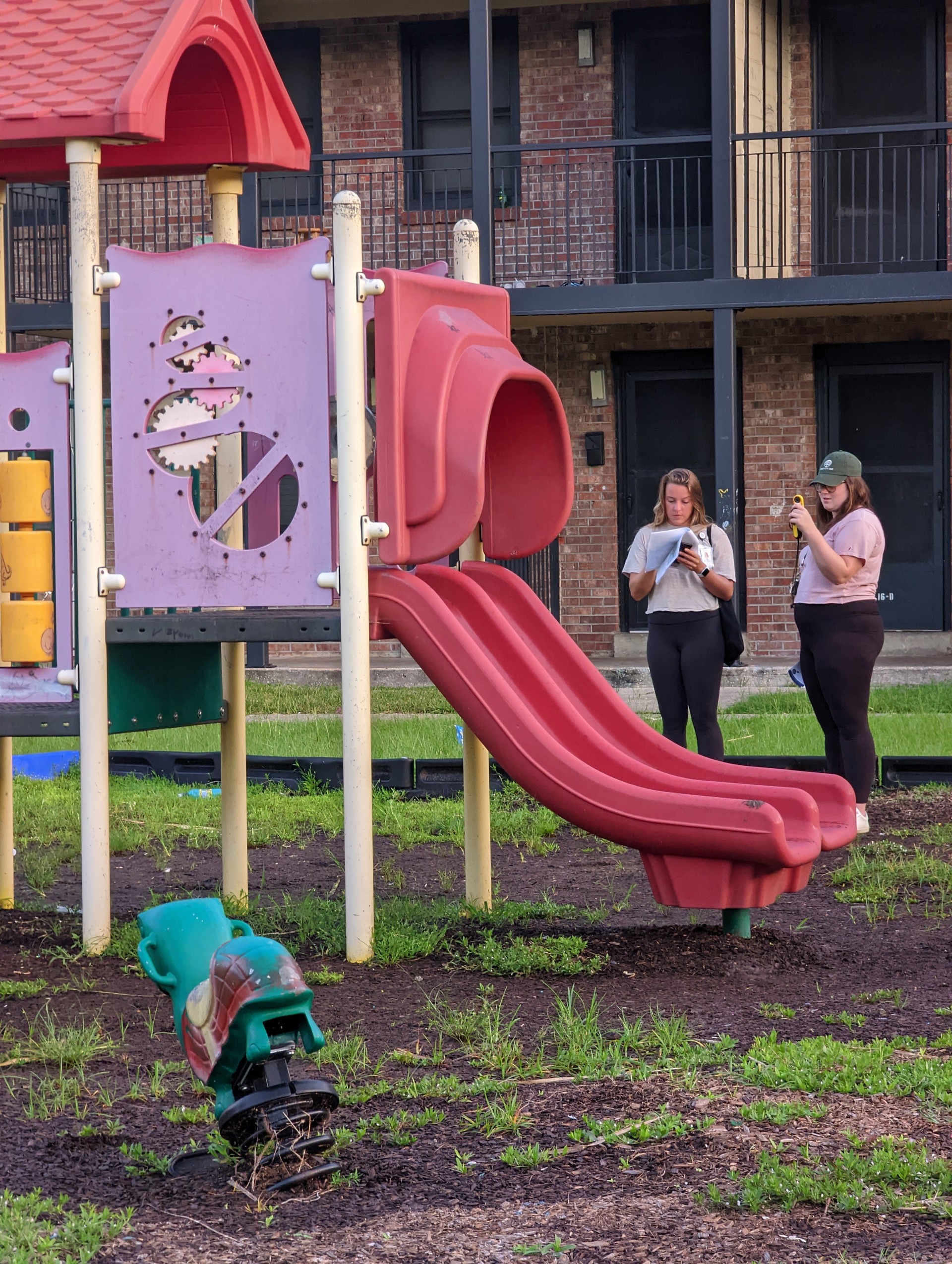 Two people standing next to a pink and red playground slide, recording temperature