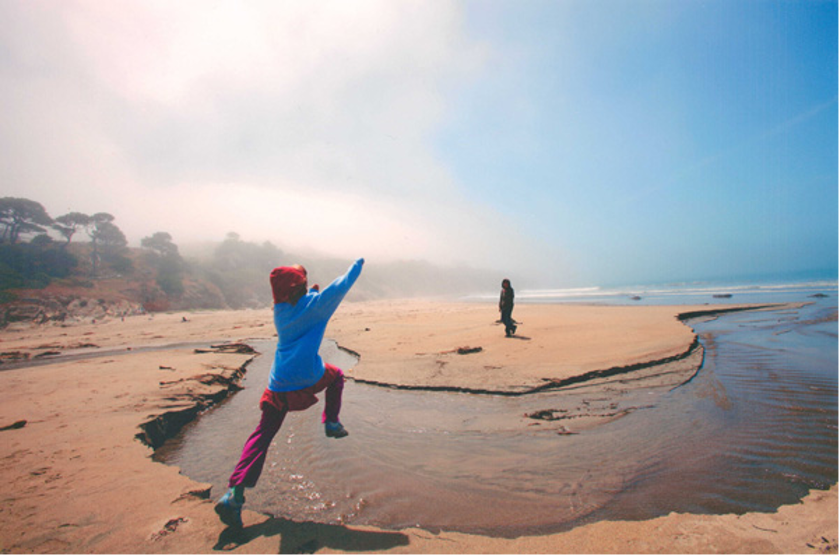 child jumping over a stream of water flowing through a beach
